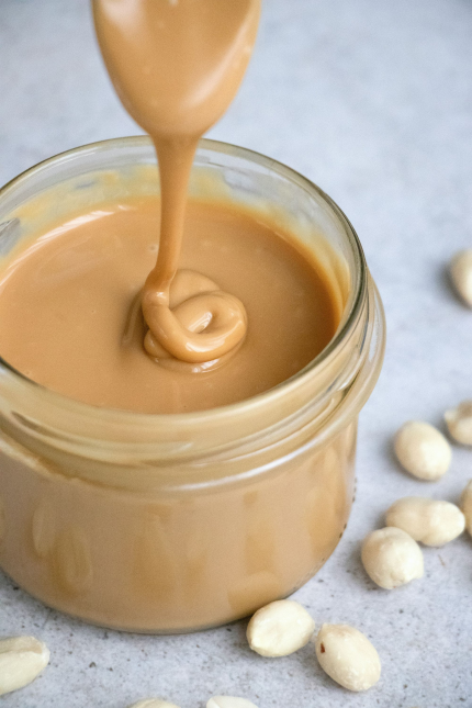 A jar of peanut butter with a spoon drizzling from above.